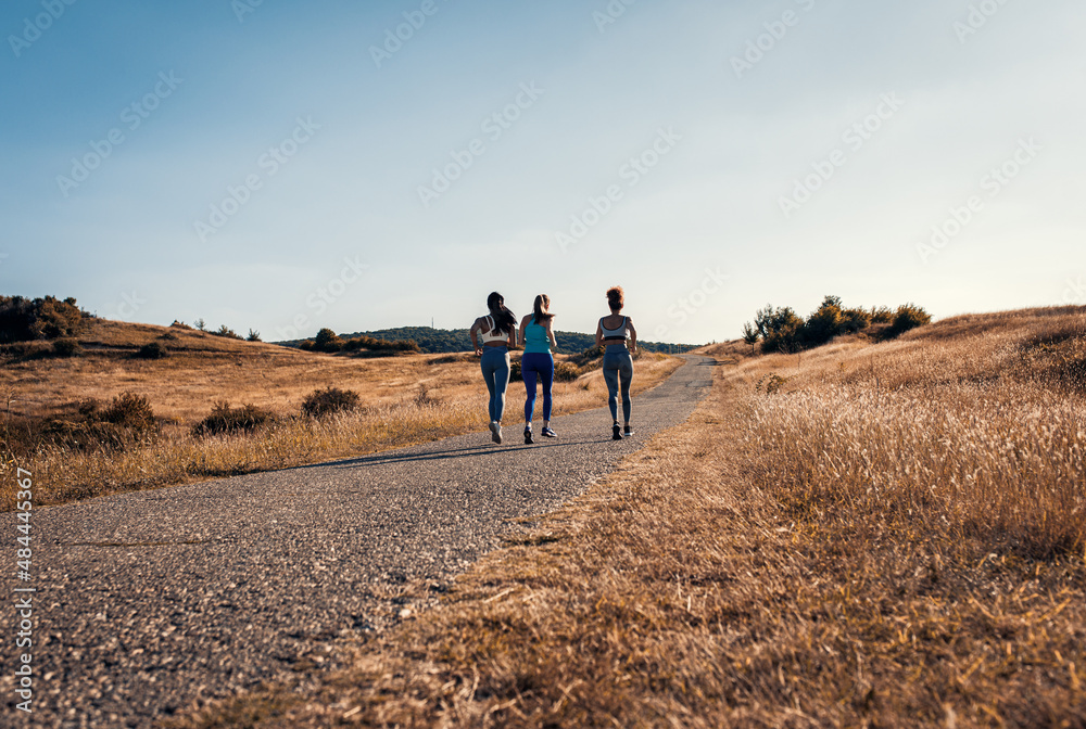 Rear view of three sporty female friends running outdoors.