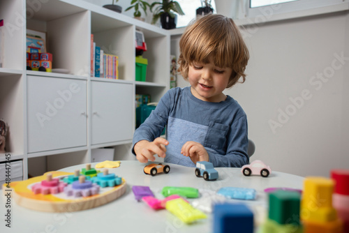 Beautiful toddler play with a wooden toys at home. Toddler play with a color educational toy and wooden car. Child play at the table in the baby room near Christmas tree. Funny baby. Lifestyle.