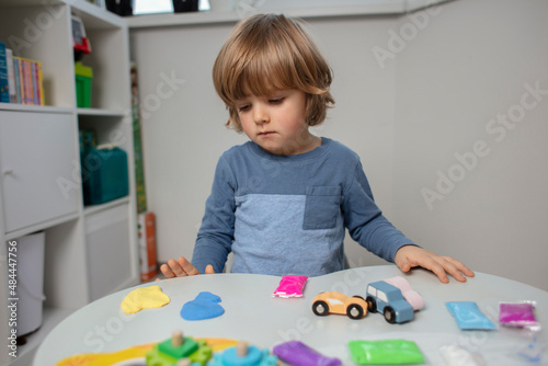 Beautiful toddler sculpt a plasticine and play with a wooden toys at home. Toddler play with a color educational toy and wooden car. Child play at the table in the baby room. Funny baby. 