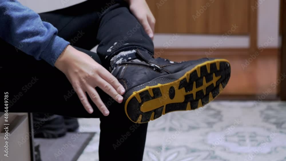 Child Takes Off His Wet Winter Shoes, Boots, with Adhering Snow in the Corridor. A tired schoolboy came home after a winter walk and took off his shoe. Close-up of the sole of the orange color. Child Takes Off His Wet Winter Shoes, Boots, with Adhering Snow in the Corridor. A tired schoolboy came home after a winter walk and took off his shoe. Close-up of the sole of the orange color.