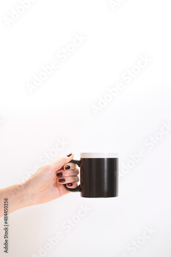 Black coffee mug mockup for design demonstration. Stylish cup mock up in female hands on white wall background.