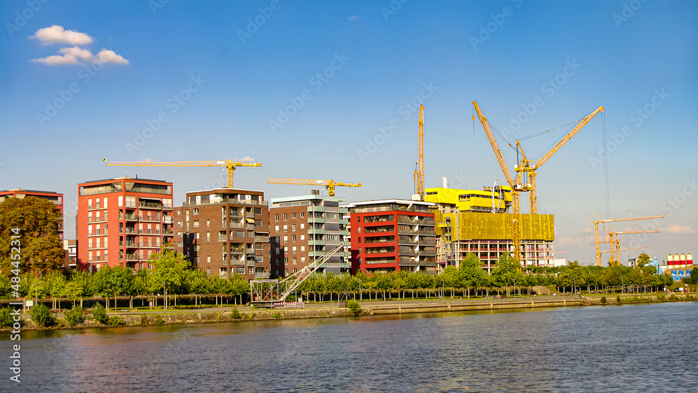 Cityscape at the bank of Main river with modern living houses construction sites in financial and historic downtown of Frankfurt, at sunset and sunny day.