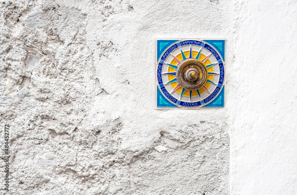 A beautiful doorbell on a plastered wall in the form of a blue square and a circle inside it with the Italian names of the winds along the outline of the circle