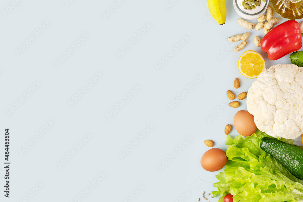 Food banner with organic vegetables and fruits, olive oil, nuts, seeds and eggs on a blue background with copy space. Concept of healthy food and diet. Foods with a lot of vitamins and nutrients