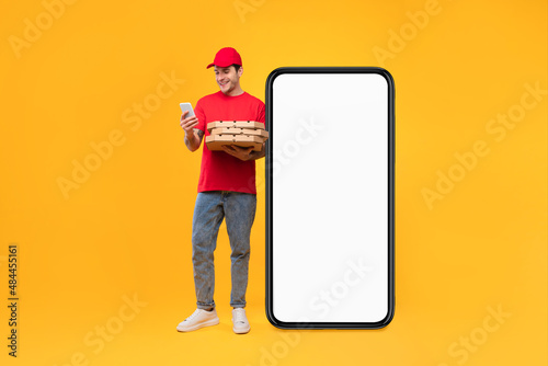 Courier Guy Near Big Smartphone Holding Pizza Boxes, Yellow Background photo