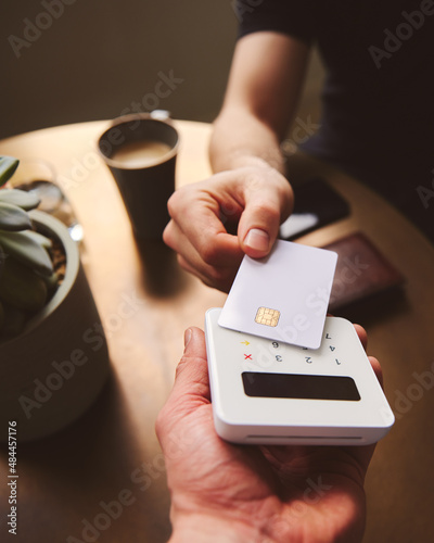 Hand tapping a credit card on a contactless card reader paying for coffee