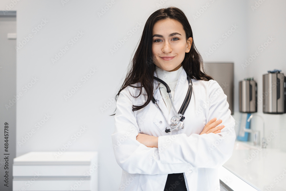Portrait of cheerful female doctor in lab coat standing with crossed hands on her office Portrait of cheerful female doctor in lab coat standing with crossed hands on her office