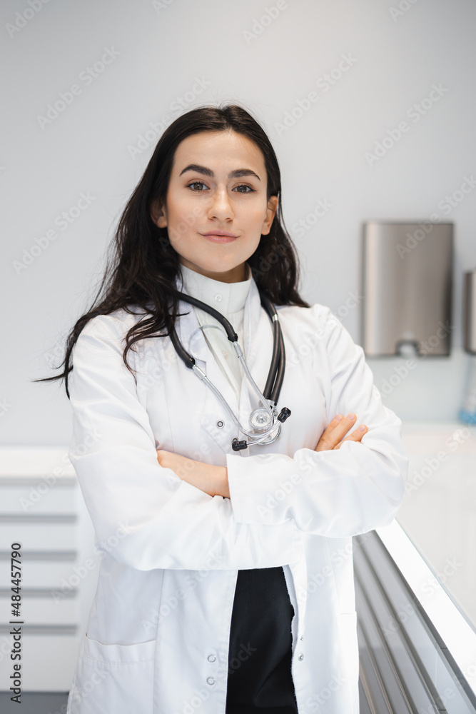 Portrait of female doctor in lab coat standing with crossed hands on her office Portrait of female doctor in lab coat standing with crossed hands on her office