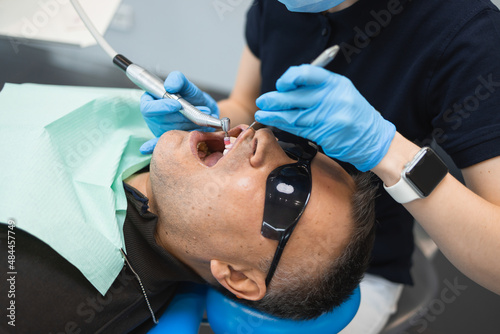 Dentist doing teeth cleaning procedure for male patient. Professional dental hygiene