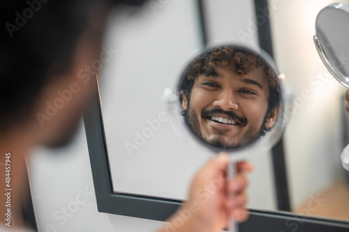 Cheerful cute male holding the handglass before his face photo
