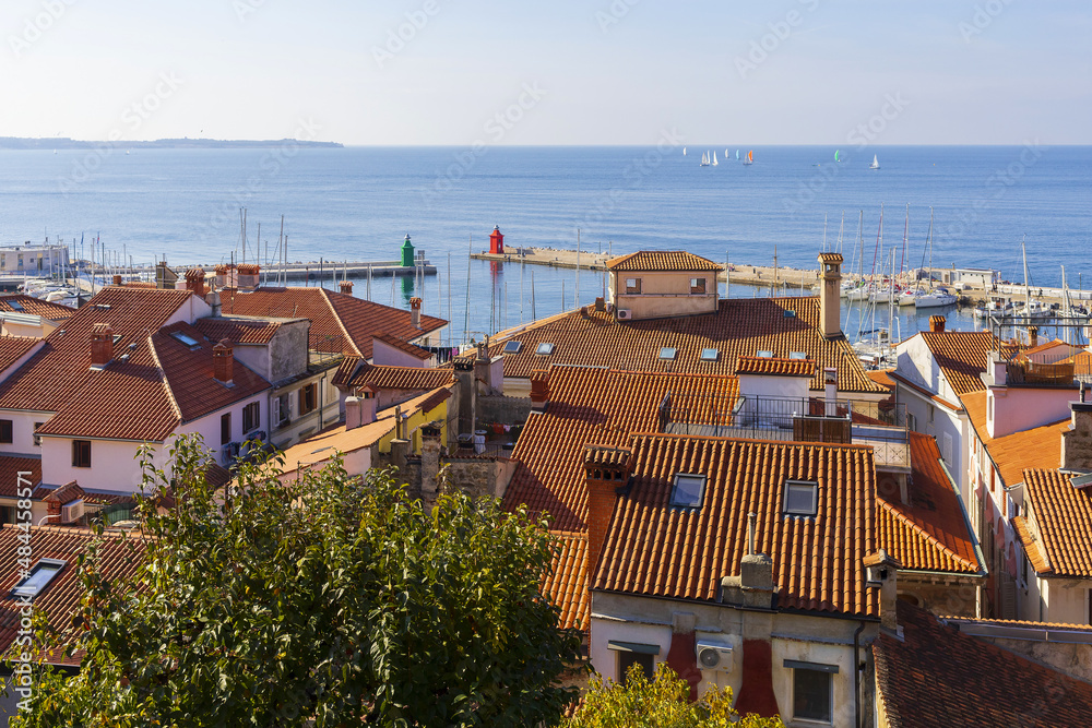 Panoramic view to red tiled roofs of ancient slovenian city of Piran with Adriatic sea on horizon under blue sky on sunny summer day