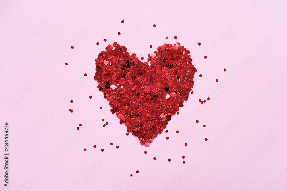 Valentine's day background. Heart made of shiny red small decorative hearts on a pink background strewn with sparkles. Flat lay, place for text.