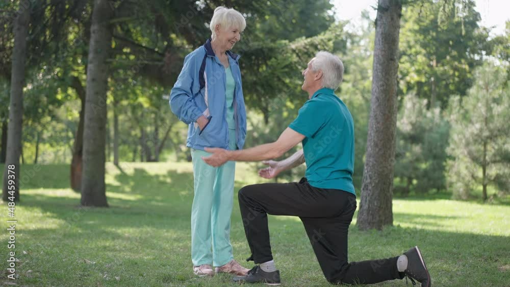 Thankful senior wife hugging husband tying shoelace on sneakers in spring summer park. Happy loving Caucasian woman embracing man in slow motion. Love and gratefulness concept Thankful senior wife hugging husband tying shoelace on sneakers in spring summer park. Happy loving Caucasian woman embracing man in slow motion. Love and gratefulness concept