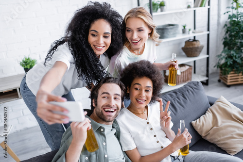 happy african american woman taking selfie with cheerful friends in living room.