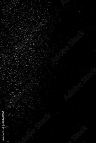 Drops of water flow down the surface of the clear glass on a black background. Vertical orientation. Texture for creativity.	