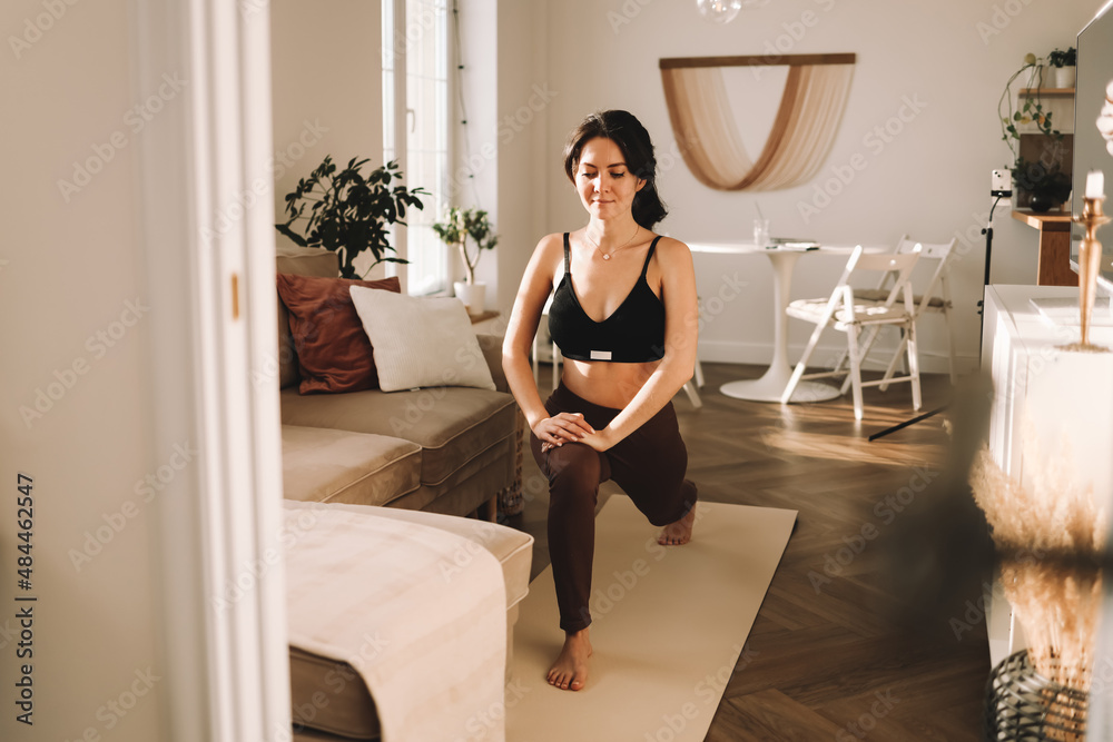 An athletic slender young woman in sportswear does sports, does physical training, yoga and stretching in a cozy living room at home in an apartment on isolation. Healthy lifestyle An athletic slender young woman in sportswear does sports, does physical training, yoga and stretching in a cozy living room at home in an apartment on isolation. Healthy lifestyle