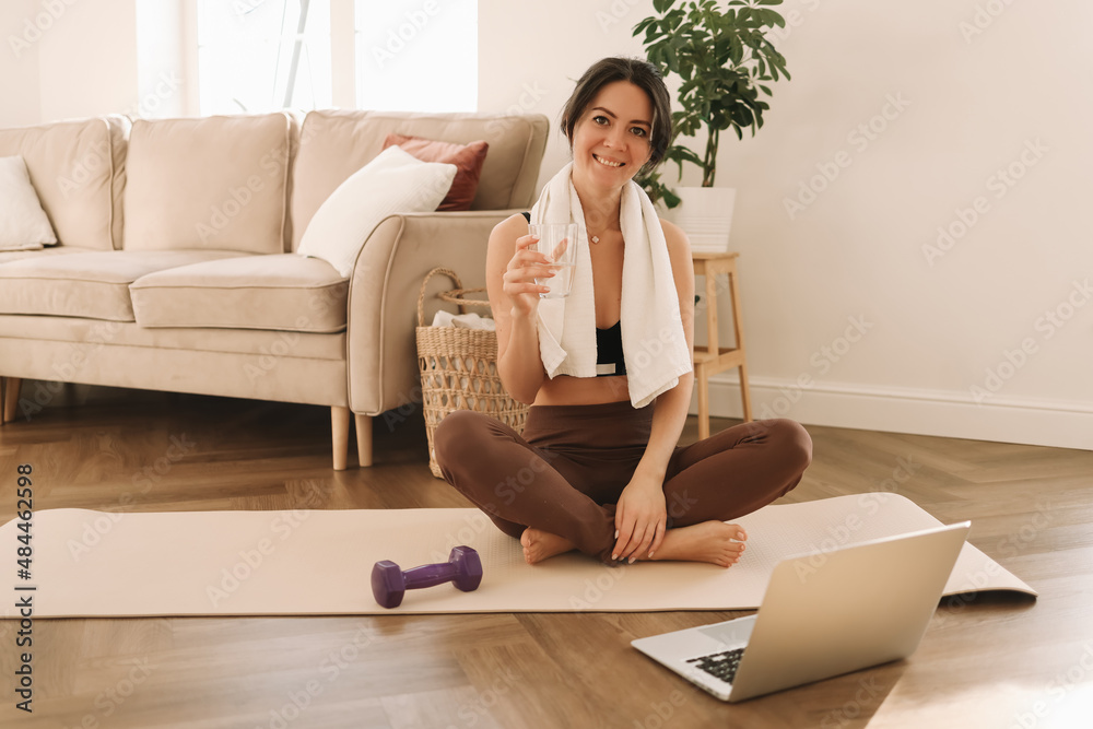 Athletic young millennial woman is engaged in sports training and exercise online in a room at home. A fitness blogger records videos during a workout using a smartphone and laptop. Selective focus Athletic young millennial woman is engaged in sports training and exercise online in a room at home. A fitness blogger records videos during a workout using a smartphone and laptop. Selective focus
