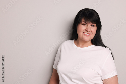 Beautiful overweight mature woman with charming smile on light grey background. Space for text