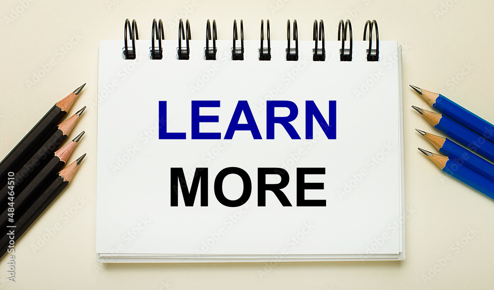 On a light background, a white notebook with the text LEARN MORE and black and blue pencils on the sides. On a light background, a white notebook with the text LEARN MORE and black and blue pencils on the sides.