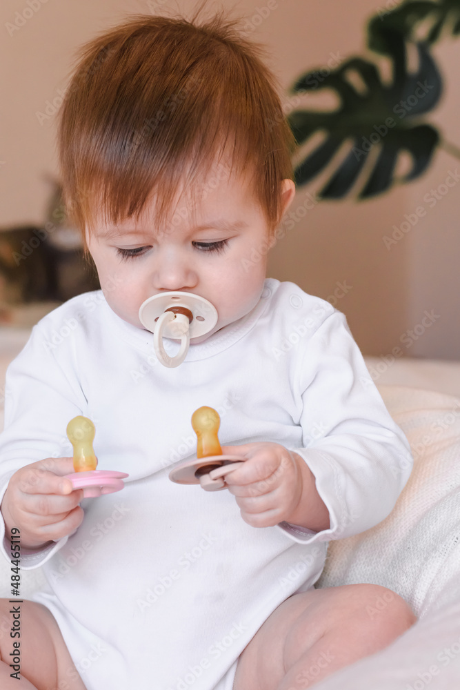 Cute baby holds nipples of different colors in his hands and one nipple pacifier in his mouth, chooses which one to take. Difficulties of choice in childhood Cute baby holds nipples of different colors in his hands and one nipple pacifier in his mouth, chooses which one to take. Difficulties of choice in childhood