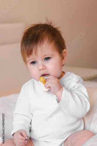 Cute baby in white body holds nipple pacifier in his hands