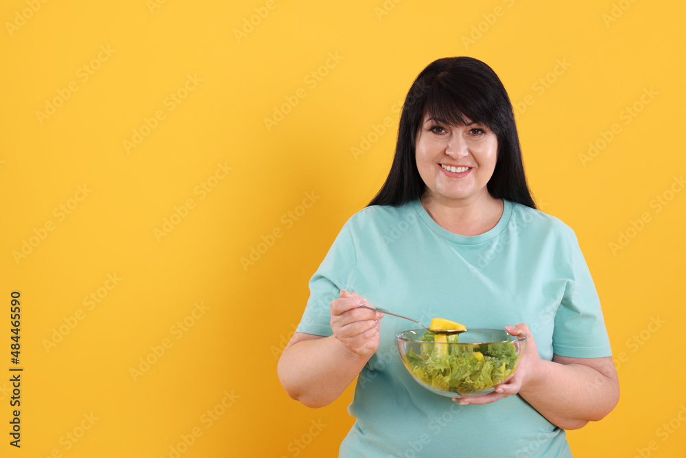 Beautiful overweight woman eating salad on yellow background, space for text. Healthy diet Beautiful overweight woman eating salad on yellow background, space for text. Healthy diet