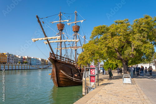 People walk the promenade and pass by the Nao Victoria replica ship docked at the Guadalquivier River in the historic central downtown area of Seville, Spain. photo