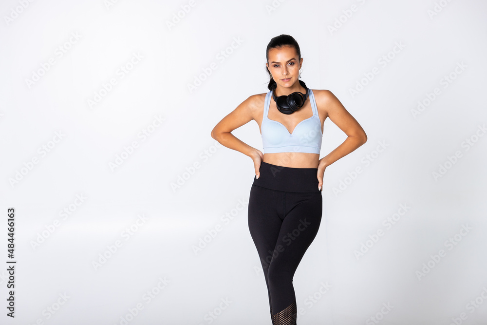 woman with headphones around her neck on white background in sport outfit with pony tail, female trainer with music gear ready for gym and workout woman with headphones around her neck on white background in sport outfit with pony tail, female trainer with music gear ready for gym and workout