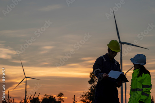 Two engineers working and holding the report at wind turbine farm Power Generator Station on mountain,Thailand people,Technician man and woman discuss about work