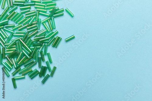 Photography Pile of green bugle beads on light blue background, flat lay