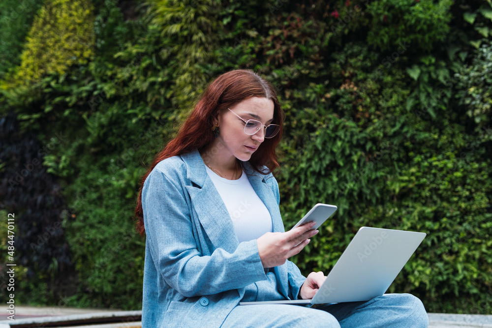 Woman reading text business message from her managers connected to public internet outdoors, beautiful professional woman chatting on cell smartphone and using laptop while relaxing outdoors Woman reading text business message from her managers connected to public internet outdoors, beautiful professional woman chatting on cell smartphone and using laptop while relaxing outdoors