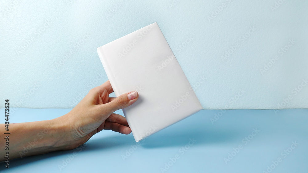 A mockup of an close book in womans hand isolated on blue .mockup with shadow. book endpaper. Blank catalog, magazines or brochure. A mockup of an close book in womans hand isolated on blue .mockup with shadow. book endpaper. Blank catalog, magazines or brochure.