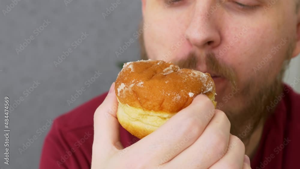 Close-up of a bearded man biting a donut with appetite eats high-calorie food. Donuts are a dangerous food that causes obesity, heart problems and diabetes Close-up of a bearded man biting a donut with appetite eats high-calorie food. Donuts are a dangerous food that causes obesity, heart problems and diabetes