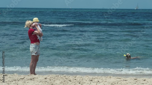 A girl with a child on vacation on the coast of Israel. The dog takes out a toy thrown by the owner into the water.
