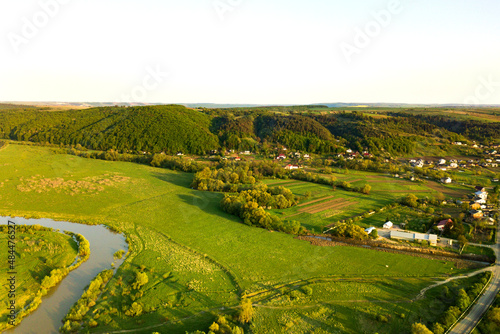 Aerial landscape view of green cultivated agricultural fields with growing crops and distant village houses on bright summer