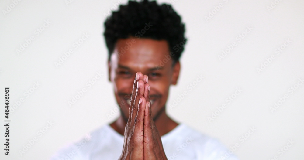 Grateful African man portrait giving thanks, faith gesture with hands smiling to camera, feeling compassion
