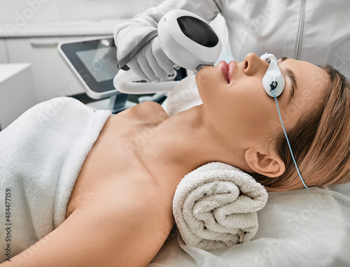 Photorejuvenation, rosacea treatment, removing brown spots and vascular mesh. Cosmetologist using IPL apparatus treats skin of female patient's face photo