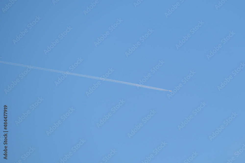Distant passenger jet plane flying on high altitude on clear blue sky leaving white smoke trace of contrail behind. Air transportation concept Distant passenger jet plane flying on high altitude on clear blue sky leaving white smoke trace of contrail behind. Air transportation concept