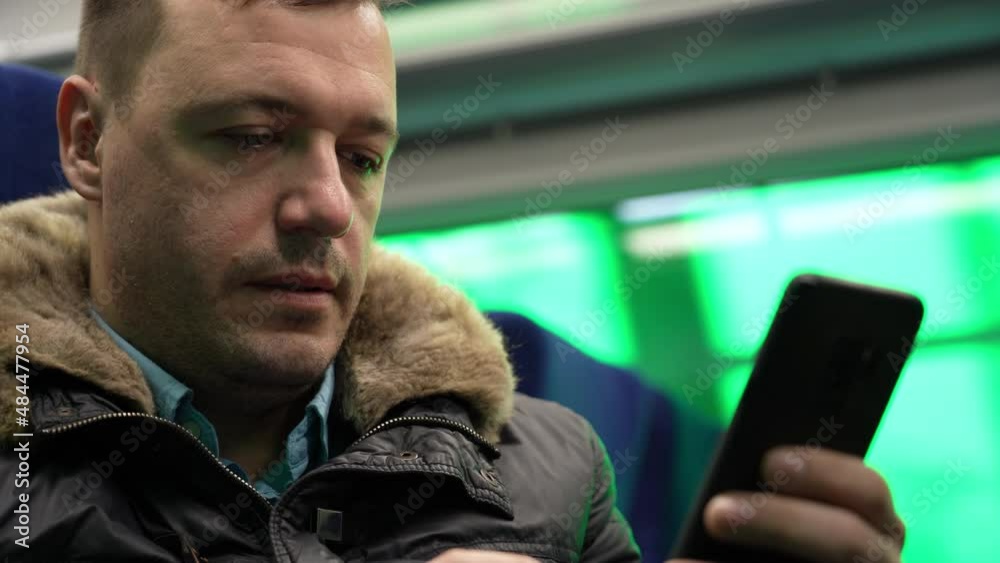 Millennial man commuting on train sitting looking social media, texting messages using cell phone while riding home by train passes through suburbs during Covid-19 or coronavirus pandemic, lockdown Millennial man commuting on train sitting looking social media, texting messages using cell phone while riding home by train passes through suburbs during Covid-19 or coronavirus pandemic, lockdown