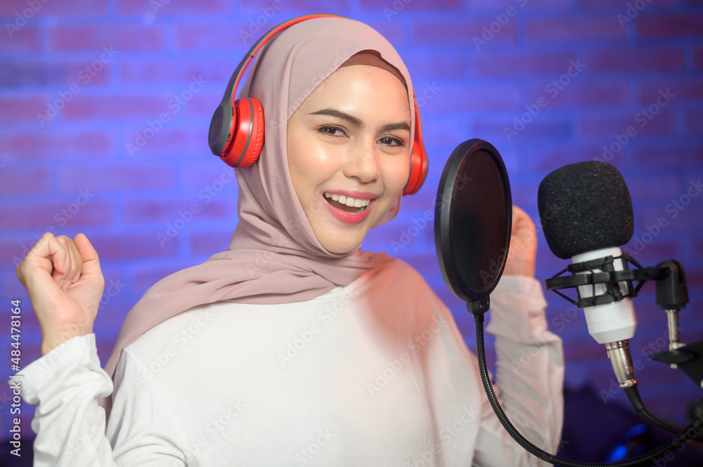Young smiling muslim female singer wearing headphones with a microphone