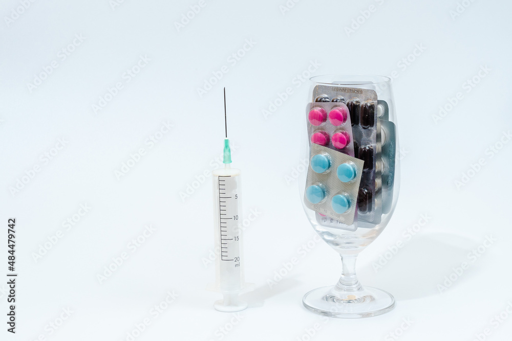 Tablets and medical capsules in glass with syringe isolated on white background Tablets and medical capsules in glass with syringe isolated on white background