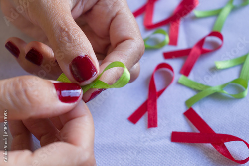 Cintas de colores, cintas para campañas de lucha contra el cáncer y el SIDA. Manos preparando cintas rojas y verdes. Campaña roja de concientización sobre el VIH photo