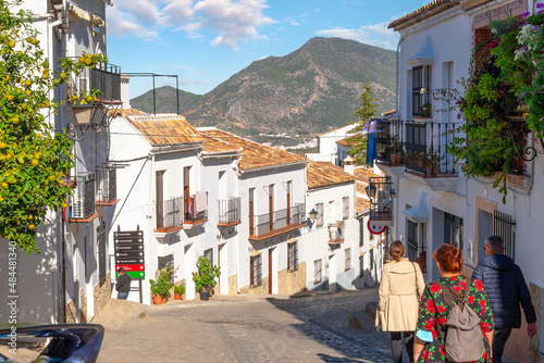 Fototapeta Naklejka Na Ścianę i Meble -  A small group of unidentifiable people walk down a typical street of homes in the Andalusian White Village of Zahara de la Sierra, Spain.