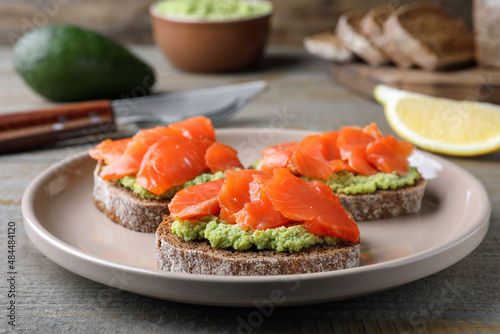 Delicious sandwiches with salmon and avocado on grey wooden table, closeup