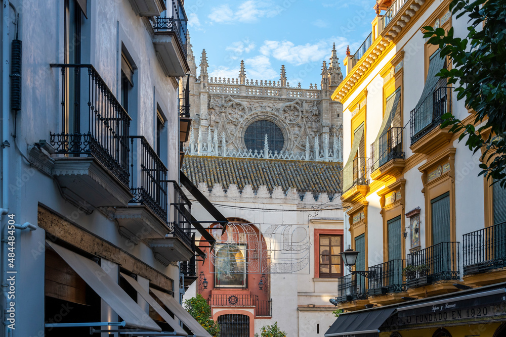 Obraz premium View of the Seville Cathedral through an alley street with buildings on either side in the Barrio Santa Cruz district of Seville, Spain.