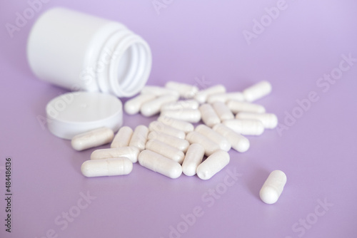 Close up white pills and capsules on purple background with copy space. Focus on foreground, soft bokeh. Pharmacy drugstore concept.