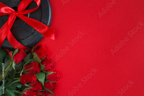 Fototapeta Naklejka Na Ścianę i Meble -  Ribbon wrapped dumbbells weight plate and roses as a love gift for Valentine's Day, birthday, anniversary, wedding. Healthy fitness gym workout flat lay composition with copy space on red background.