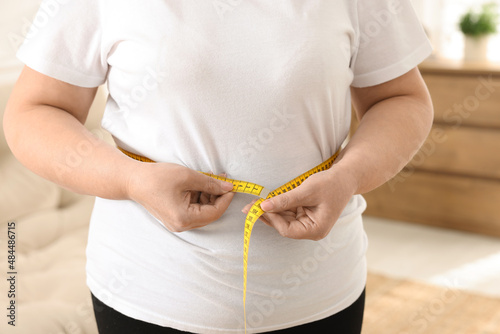 Schilderij op canvas Overweight woman measuring waist with tape at home, closeup