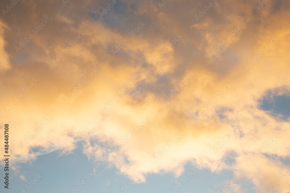The background of a blue dramatic sky with yellow clouds illuminated by the sunny evening light.