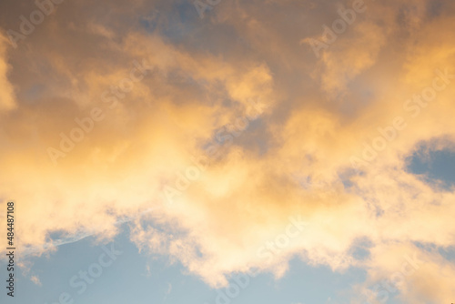 The background of a blue dramatic sky with yellow clouds illuminated by the sunny evening light.